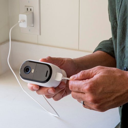 Someone is holding Arlo Essential Camera 2K while putting the charge cable to it